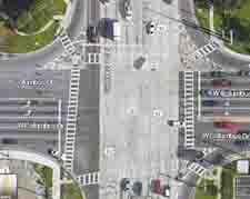 Aerial view of a Google Maps image of a 4 leg intersection with 6 and 8 lane crossings, islands separating the right-turning lanes on the top two and bottom right crossings, and skewed crosswalks.